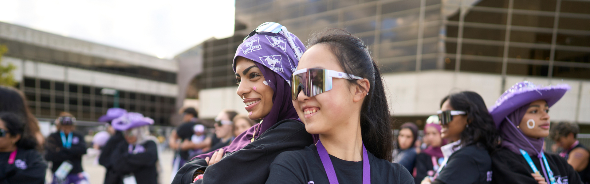 Two young women stand back to back smiling confidently.