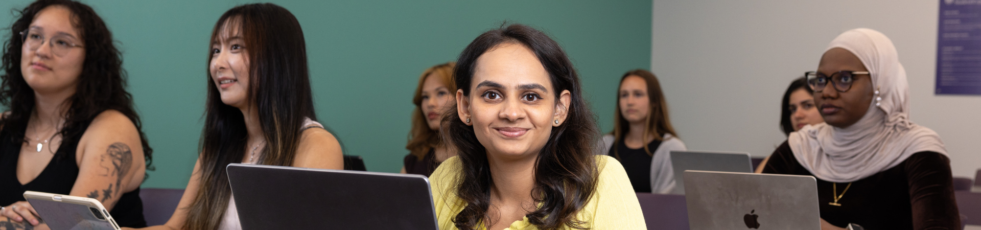 A young woman sits in a classroom setting on a laptop.